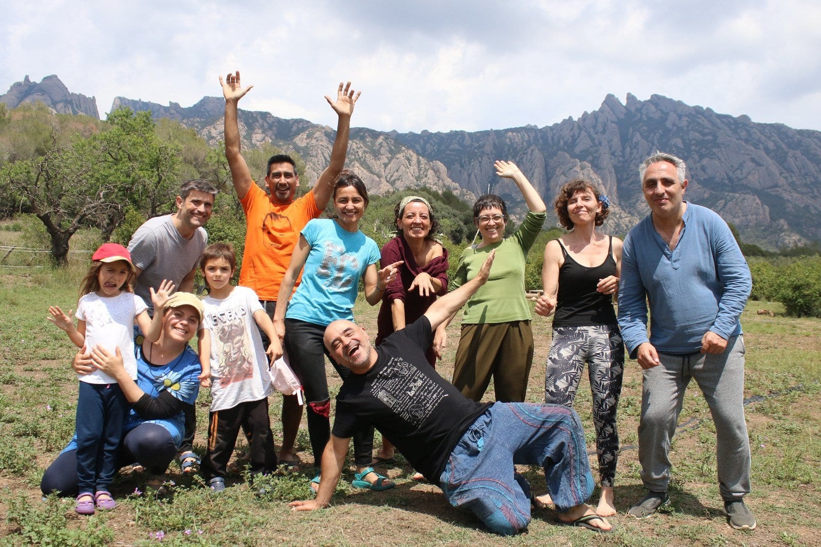 Un grupo de personas, entre adultos y niños, posan y sonríen enérgicamente al aire libre frente a una cadena montañosa en un día nublado.