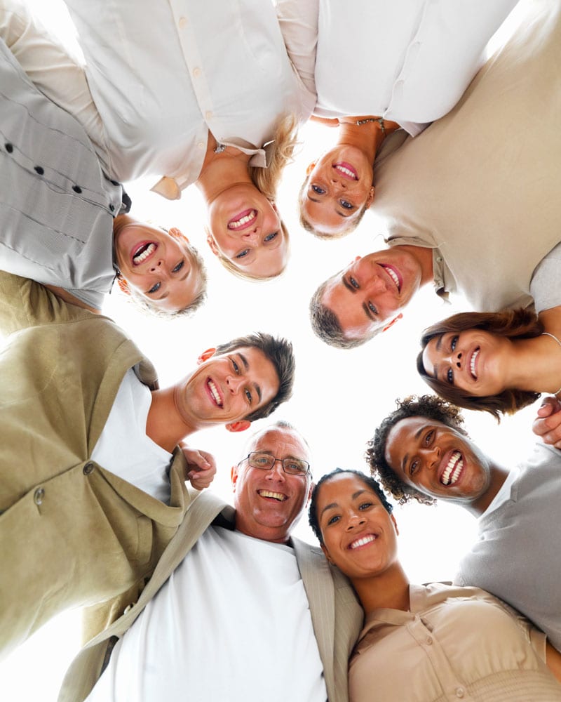 Grupo diverso de personas sonriendo y mirando hacia abajo en círculo.