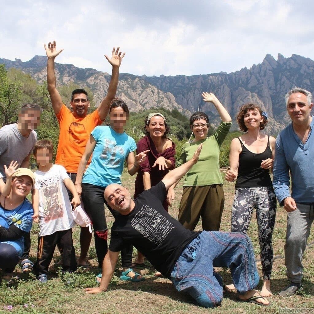 Un grupo de diez personas, entre las que hay niños con la cara borrosa, posan y sonríen al aire libre con las montañas de fondo.