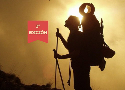 Un excursionista con una gran mochila y bastones se encuentra en una ladera al atardecer. En una placa se lee "3ª Edición" en español.