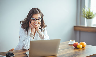 Mujer sonriente usando laptop en oficina con frutas y plantas.