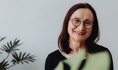 Mujer sonriente con gafas y cabello castaño oscuro en fondo neutro.