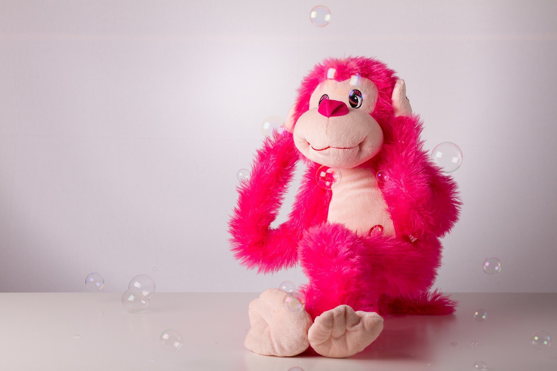 Un juguete de felpa rosa brillante se sienta sobre una superficie blanca con burbujas translúcidas flotando a su alrededor, perfecto para reconfortar a los niños que aprenden cómo escuchar un no sin sufrir, sobre un fondo gris claro.