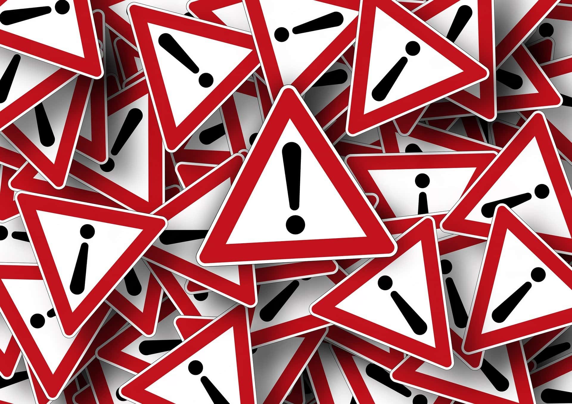 Un montón de señales de advertencia triangulares superpuestas con signos de exclamación, cada una bordeada en rojo y blanco.